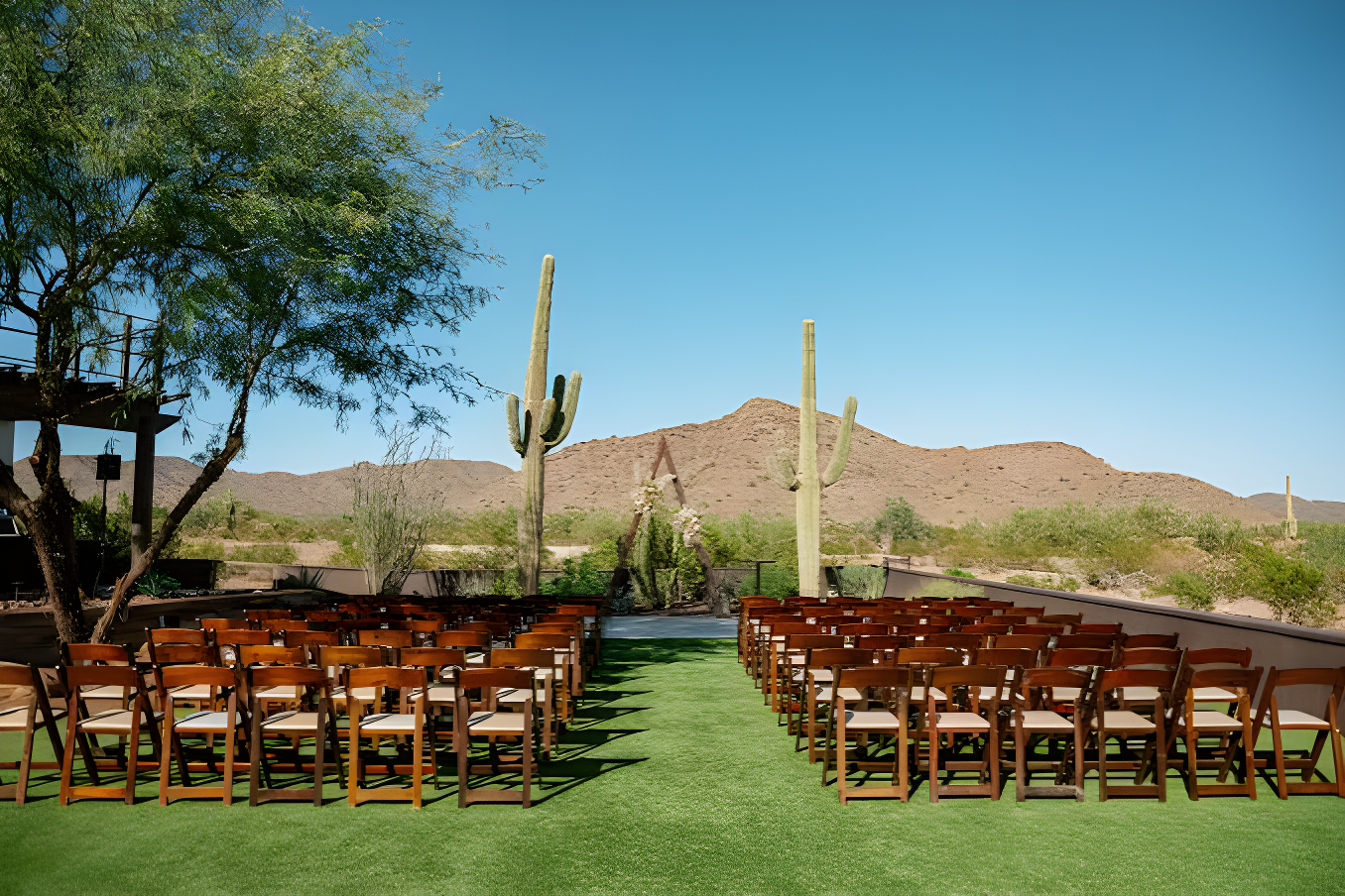 Floral-topped arbor between two saguaro cacti at the end of the empty ceremony aisle